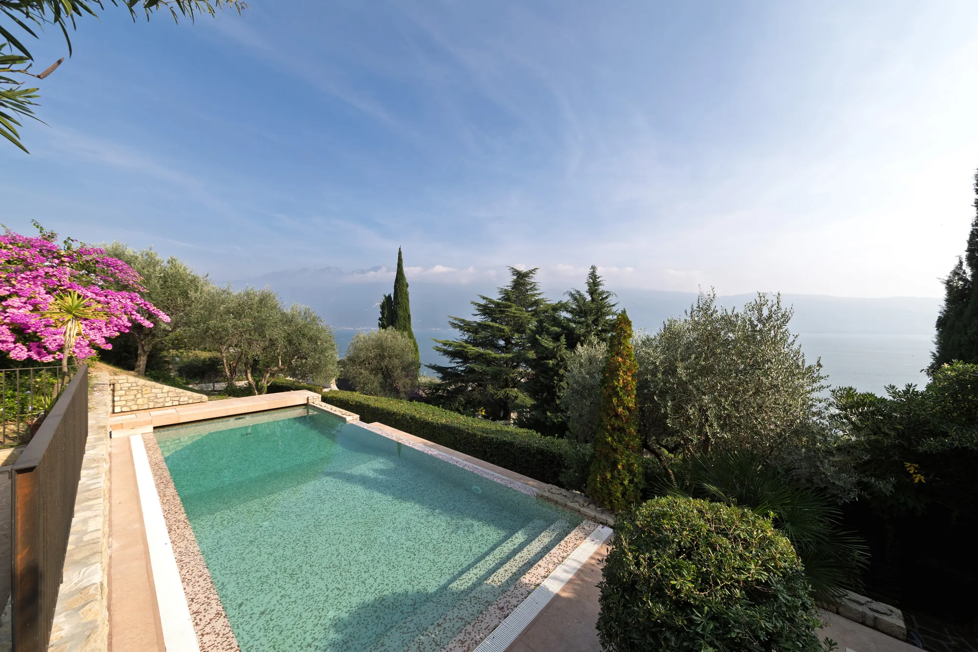 Swimming pool framed by olive trees and cypresses with a view of Lake Garda